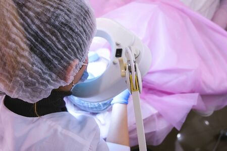 Cosmetologist at work. Treats the patients skin with a large glowing magnifying glass. Face cleaning