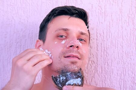 Portrait of young handsome man is applying fresh homemade coconut mask on the face. Natural organic cosmetics for skin care.の写真素材
