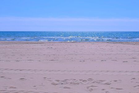 Warm and clear weather at seaside. Sea sand beach with blue water and foamy waves at sunny day....
