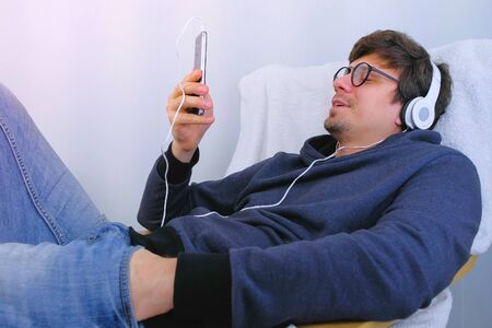 Man listens music in headphones on smartphone and sings a song in karaoke. Relax time in armchairの写真素材