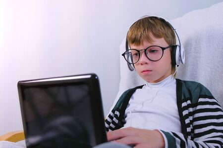 Boy in glasses and earphones is writing on laptop. Online study and learning