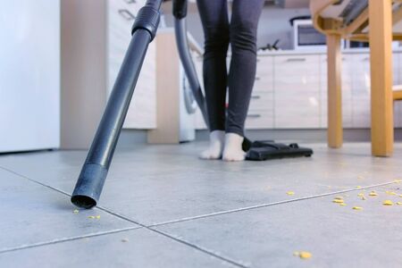 Woman vacuuming the kitchen floor without brush, only pipe. Legs close-upの写真素材