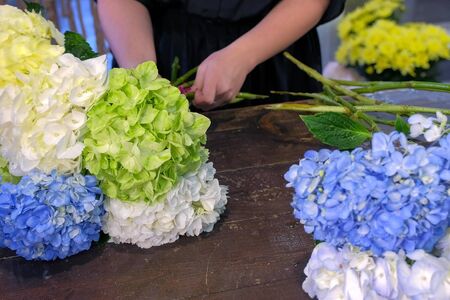 Floral business concept. Florist woman makes bouquet of blue, yellow and green hydrangea flowers in shop for sale, flowers closeup. Working in floristic studio store. Creating professional bouquet.の写真素材