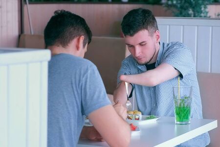 Independent Invalid with disabilities. Disabled man with two amputated stump hands meets friend eats...