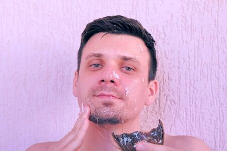 Portrait of young handsome man is applying fresh homemade coconut mask on the face from coconut shell. Natural organic cosmetics for skin care.の写真素材