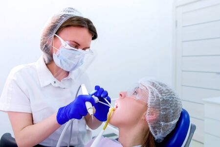 Dentist hygienist makes ultrasonic teeth cleaning for young woman in dentistry. Patient visit dentist on ultrasound teeth brushing procedure in stomatology clinic. Uses salvia ejector. Oral hygiene.の写真素材