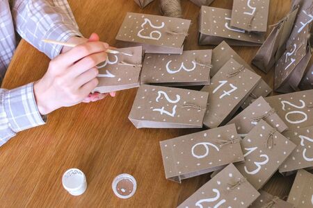 Woman makes christmas advent calendar. Writes a number on the bag by brush and white paintの写真素材