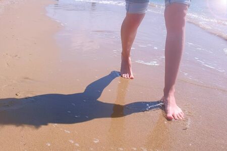 Girl tourist on trip in vacation. Barefooted woman traveller walks in water on sea sand beach, legs closeup. Feet on ocean water and sand shore with small waves. Travel tourism rest sea concept.の写真素材