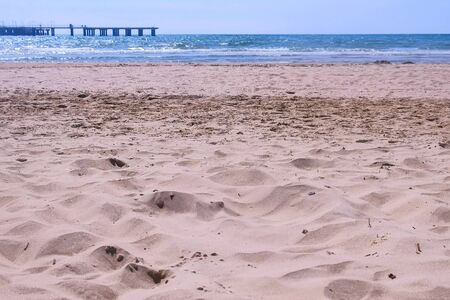 Sea sand beach with stormy waves and pier view at sunny windy day. Beautiful nature background.