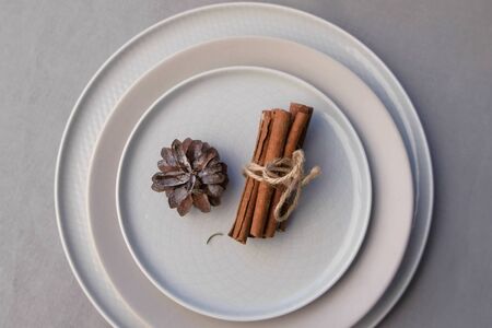 Plates for Christmas dinner on table decorated with pine cone and cinnamon sticks. Minimalism style. Beautiful festive table setting. Xmas and New Year traditions in winter hoidays.の写真素材