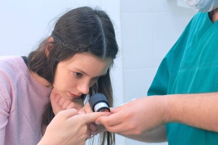 Surgeon and patient woman examine wart on finger of using dermatoscope magnifier before laser removing. Inspecting verruca on hand, cure and treatment. One day surgery concept.の写真素材