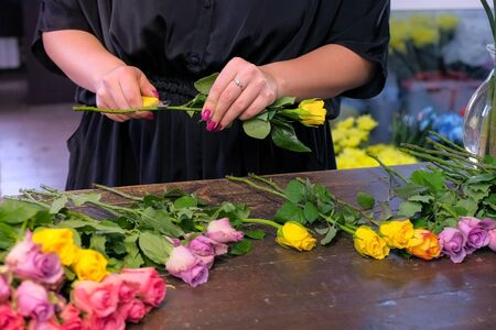 Floral business concept. Professional florist woman prepares flowers to bunch bouquet. She cuts rose thorns in shop, closeup hands. Working day in floristic studo store salon.の写真素材