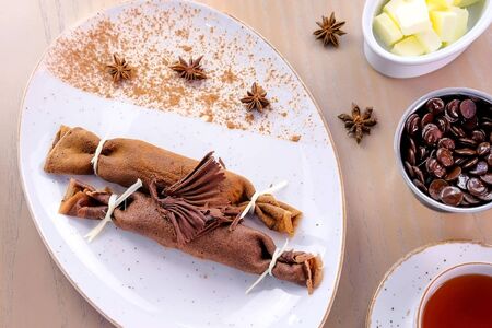 Chocolate russian pancakes, blini with curd filling on the plate. Served with a cup of tea and chocolate. Top viewの写真素材