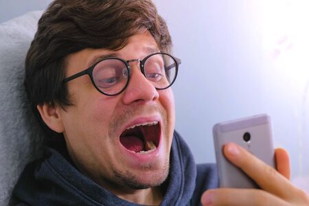 Man in glasses examines his teeth through the camera on the mobile phoneの写真素材