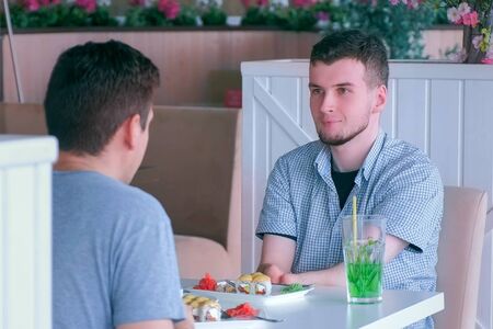 Problem of adaptation to usual life guy without wrists. Disabled man with two amputated stump hands meets friend and talks having lunch in cafe. Friend support communication. Person with disabilities.の写真素材