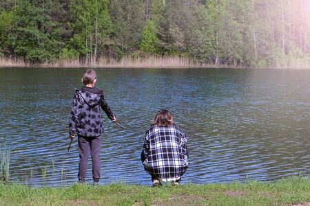 Mom and son resting on riverbank near forest at spring warm day, back view. Relaxing on nature at weekend. North summer nature. Family time together in beautiful place. Woman and child boy.の写真素材