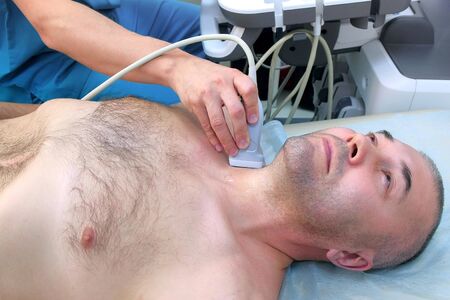 Checkup and scanning of thyroid gland at ultrasound scanner in hospital to man patient. Doctor runs ultrasound sensor over patients neck. Diagnostic procedure in clinic.の写真素材