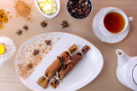 Chocolate russian pancakes, blini with curd filling on the plate. Served with a cup of tea and chocolateの写真素材