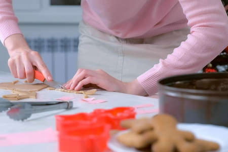 Woman is cutting parts for gingerbread house from dough and putting it in baking tray, hands...