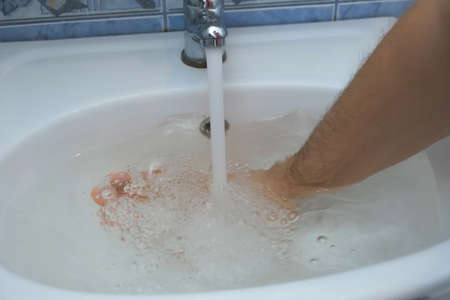 Man is trying to clean drain hole in sink which is clogged and collecting water. Water pours into a...