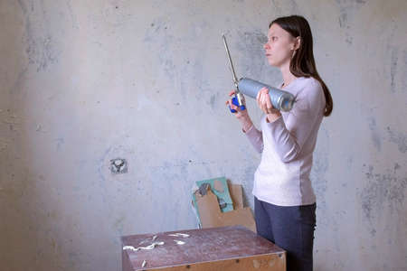 Woman trying how to mounting foam equipment working, renovation in room. She presses the tool and...