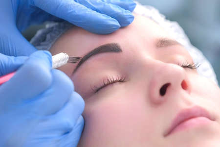 Beautician is painting shaping contour using manual tool for tattoo, womans face closeup....