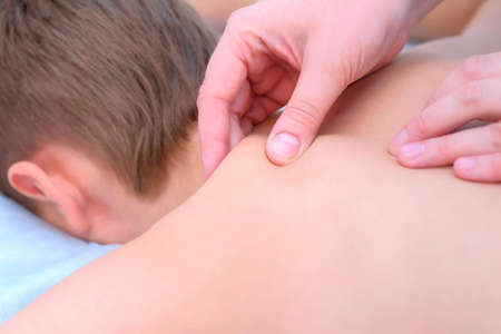 Doctor massagist making therapeutic massage to teen boy on spine, shouders and neck in clinic,...