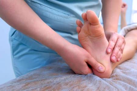 Doctor massagist making therapy massage to child boy on foot in clinic, closeup view. Dystrophy, muscle weakness, Morphan syndrome. Rehabilitation medicine, hypertonicity treatment for children.の写真素材
