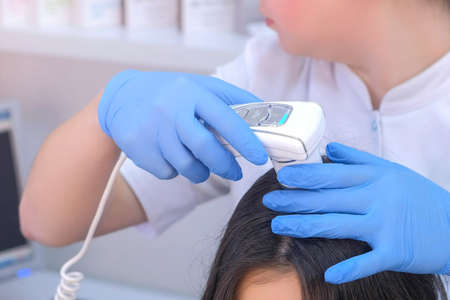 Doctor trichologist examines woman patients hairs using dermatoscope in clinic, hands closeup. Dermatologist is working in clinic on modern equipment. Medicine and healthcare concept.の写真素材