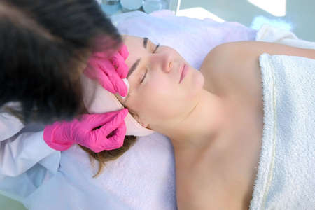 Cosmetologist is poking acne on womans face using needle and wiping cotton pads. Mechanical cleaning...