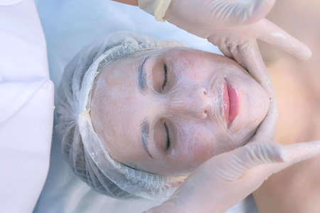 Beautician is making facial massage with moisturizing mask on woman face, closeup portrait, top...