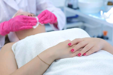 Cosmetologist making peeling to woman patients face wiping cotton pads, closeup view. Portrait of young girl on cleaning skin procedure by woman beautician in beauty clinic. Beauty industry concept.の写真素材