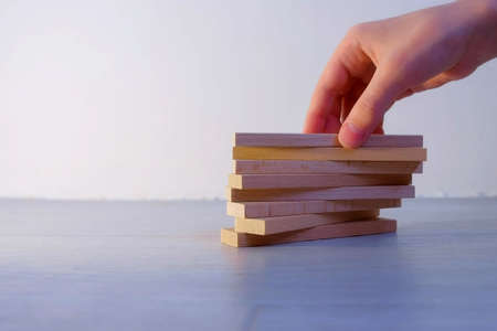Hand of man builds tower of flat wooden blocks of dice piling them on top of each other on white background. Concept of building and achieving the goal.の写真素材