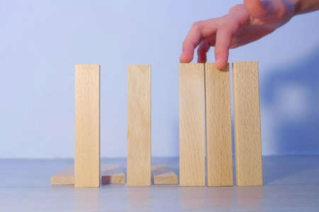 Man drops wooden blocks in row as fence via one, hand closeup view. Falling blocks in a row.の写真素材
