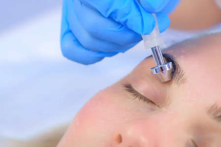 Microcurrent face treatment with hyaluronic acid gel for young woman in beauty clinic, closeup eyes....