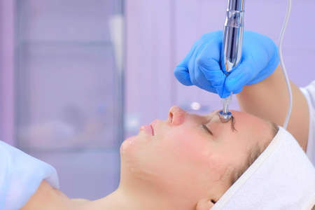 Microcurrent face treatment with hyaluronic acid gel for young woman in beauty clinic, side view....