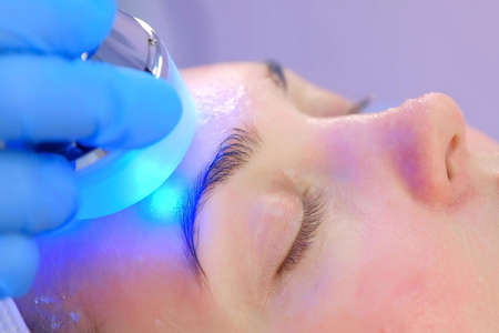 Portrait of woman on apparatus hardware phonophoresis face procedure with hyaluronic acid gel in...