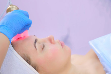 Cosmetologist doctor making phonophoresis procedure on woman face with hyaluronic acid gel, side...