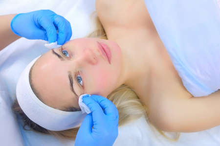 Cosmetologist doctor wiping womans face using antibacterial napkins, top view. Doctor is making...