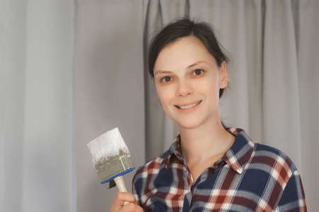 Portrait of woman house painter is looking at camera and smiling doing renovation with brush in her hand, DIY project. Professional decorator at work in object at apartment, house.の写真素材