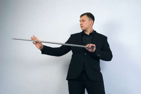 Illusionist is doing magic trick on grey background. Magician man in black suit is showing trick...