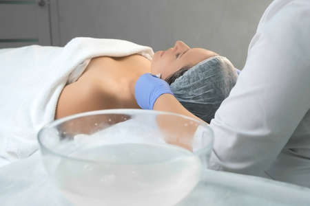 Cosmetologist doctor wiping womans face using antibacterial napkins after peeling, view from back....