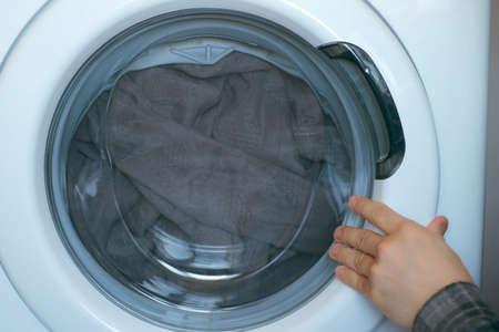 Mans hands loading the washing machine with bedspread, laundry at home. Man is doing his laundry and...