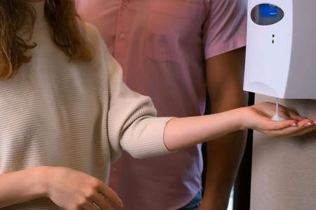 Woman is washing hands using automatic alcoholic sanitizer dispensary in a public place. Covid-19...