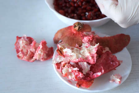 Womans hands in gloves peeling cleaning a pomegranate over the plate on table and putting peels on...
