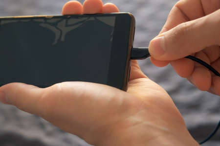 Man inserts a cable into a mobile phone for charging, hands closeup view. Inserting a charger into a...