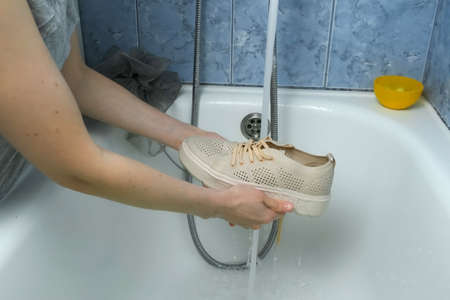 Woman is washing sport shoes in bathroom by hands, closeup hands. Laundry by hands. She is cleaning her dirty sneakers rinses under a stream of clean water.の写真素材