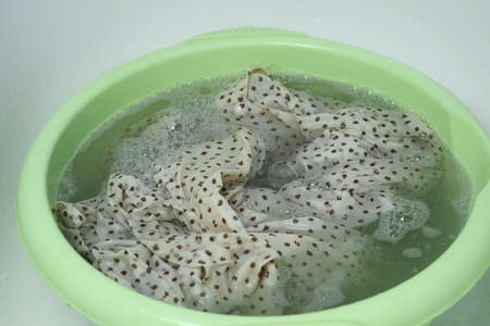 Washing dress from delicate fabric in basin in soapy water with washing powder, laundry by hands at home bathroom, closeup view. Washing at home, housekeeping and housework.の写真素材