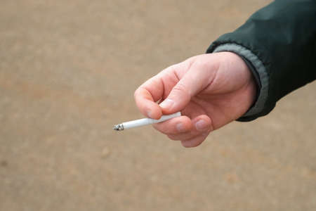 Tobacco smoke addiction, unhealthy lifestyle concept. Mans hand with a smoldering cigarette smoking a bad habit. Man is holding a burning cigarette while smoking.の写真素材