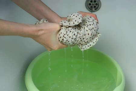 A woman wrings out a hand-washed dress over a basin, closeup view. Laundry, washing by hands. Washing at home, housekeeping and housework.の写真素材